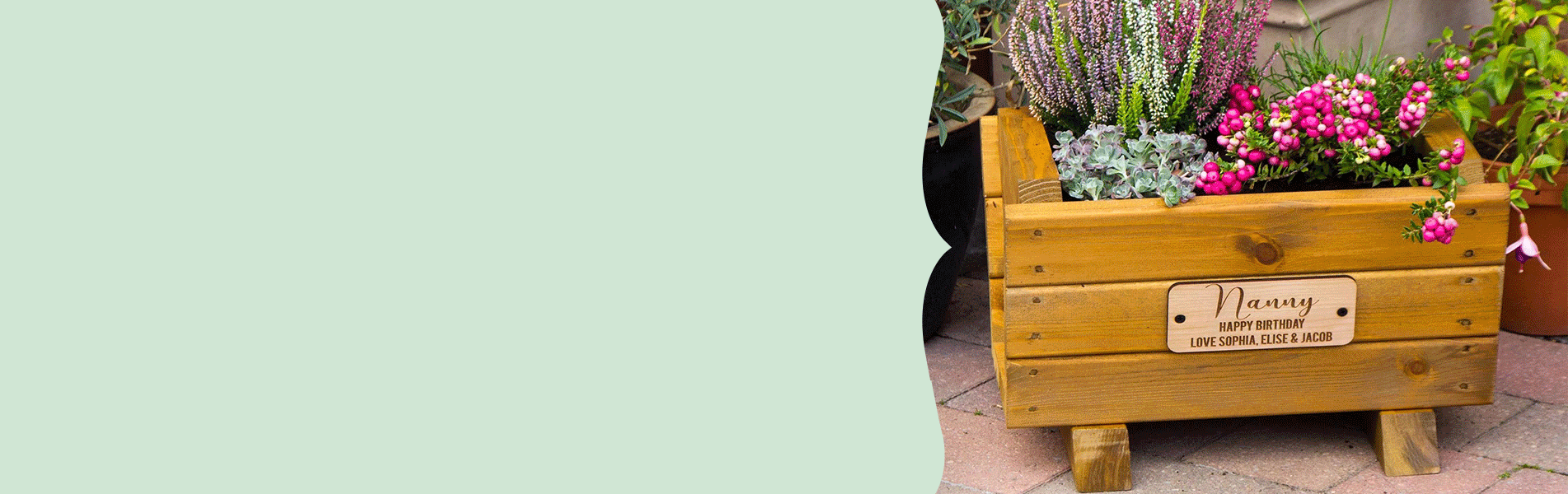 Personalised wooden flower planter with engraved plaque, surrounded by spring flowers